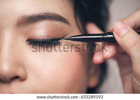 Close-up portrait of beautiful girl touching black eyeliner to her eyelid with closed eyes. Royalty-Free Stock Photo #633289592