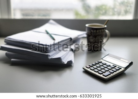 Calculator, coffee cup and papers on table beside the window