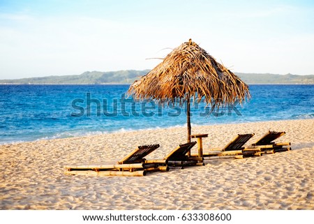 Sunbed and nipa sun umbrella on the white sand beach during sunset