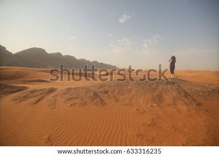 a lady photographer standing in mountain area, desert and sky background. United Arab Emirates.