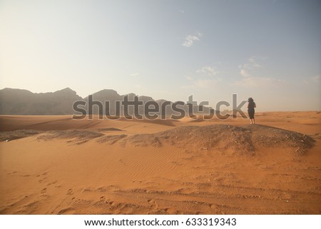 a lady photographer standing in mountain area, desert and sky background. United Arab Emirates.