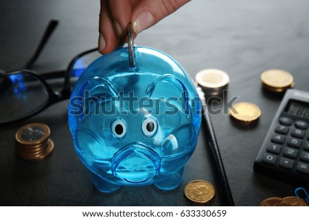 Female hand putting coin into piggy bank on grey table