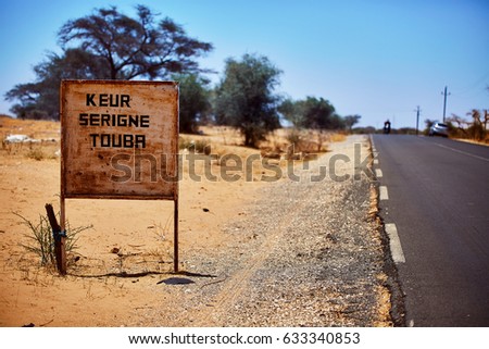 signpost to touba in senegal, background blurry desert landscape