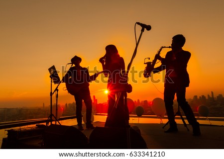 Silhouette autumn or summer scene of 1 woman and 2 men trio musician before twilight time on sky. Trio band showing on sunset light background, Bangkok Thailand