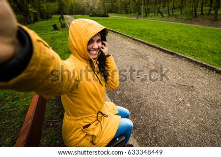 Cute happy young woman in hood taking selfie in windy day