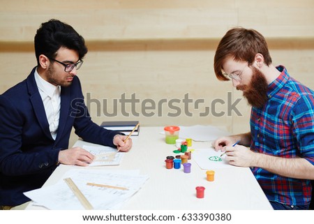 War of logic vs creativity: concentrated office worker in suit wrapped up in drawing architecture project with pencil and ruler while other man in casualwear creating picture with brush and gouache