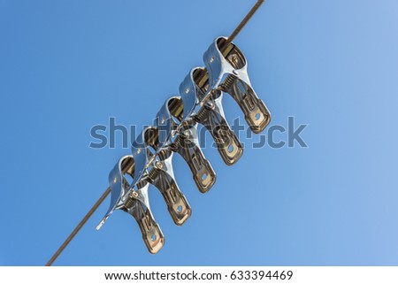 Stainless steel clothes pegs on rustic steel cable background blue sky