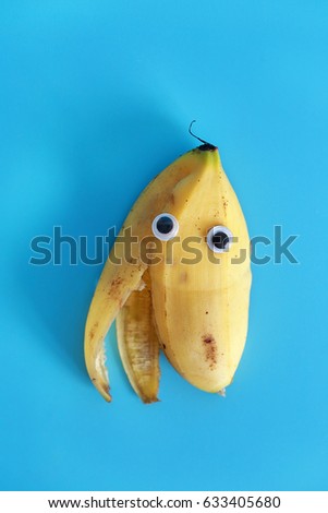 Cute and funny cartoon eyes on banana skin isolated on blue background. Mascot with big eyes