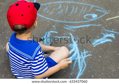 A little boy paints with chalk on the asphalt.