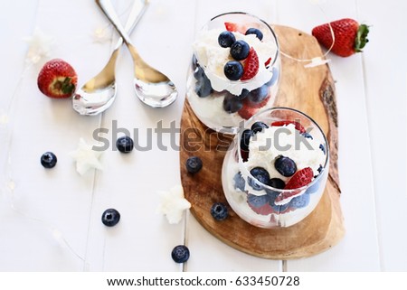 Trifles made with blueberries, strawberries, whipped cream and star shaped pound cake against a white wood background. Perfect for fourth of July. Shallow depth of field with selective focus.