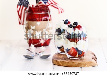 Trifle made with blueberries, strawberries, whipped cream and star shaped pound cake with American flags in background. Shallow depth of field with selective focus.
