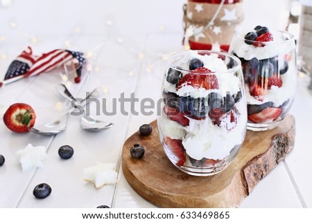 Trifles made with blueberries, strawberries, whipped cream and star shaped pound cake against a white wood background. Perfect for fourth of July. Shallow depth of field with selective focus.