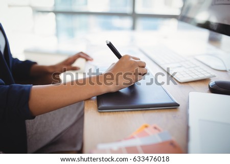 Mid section of graphic designer using graphic tablet at desk in office