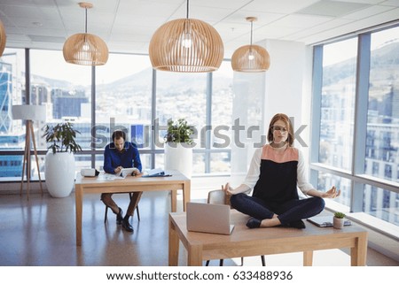 Executive meditating on desk with her colleague working in background