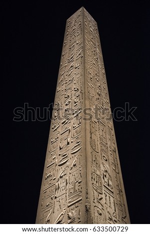 Tall stone ancient egyptian obelisk at Luxor Temple lit up in night on black sky background