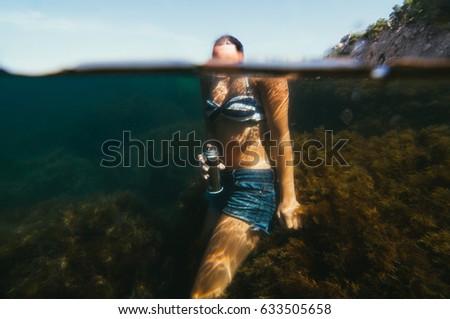Young woman in jeans shorts underwater floating with pink graffiti spray in hand