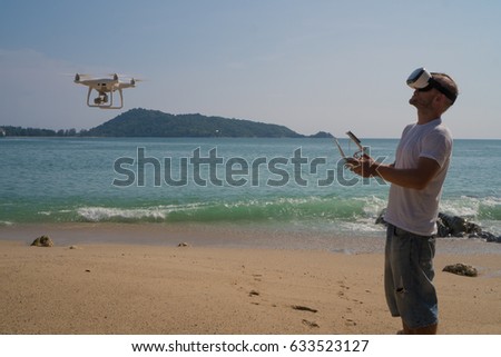 Young man wearing virtual reality glasses standing on the beach with remote controller of drone over sea and sky background