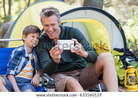 Happy father and son taking selfie by tent in forest