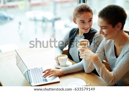 Attractive young women drinking delicious cappuccino and chatting animatedly while gathered together in coffeehouse, waist-up portrait
