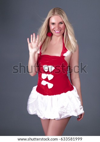 Happy smiling European blonde woman dressed Santa Claus costume and waving in front the grey background. Happy woman, Merry Christmas and winter concept.