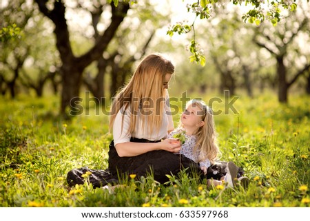 Mother with daughter a little blond girl, sitting in the garden or park on the grass, love, family, communication