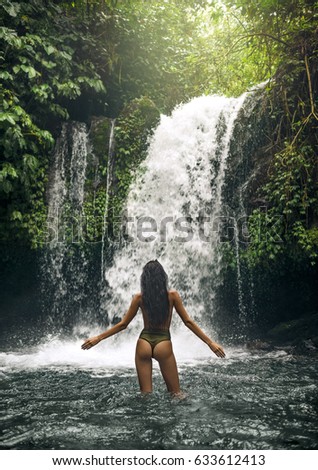 BEAUTIFUL BRUNETTE WOMAN  IN GREEN SWIMWEAR  STANDING BY TROPICAL WATERFALL

