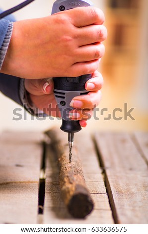 A closeup of a hardworker man drilling a wood stick with his drill on a wooden background