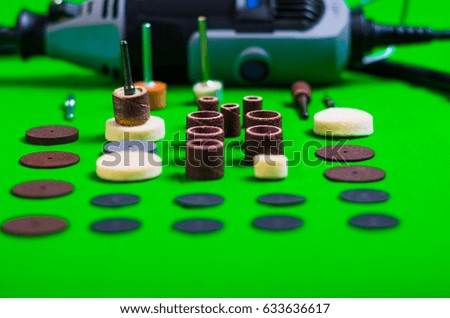A gray drill behind of the drilling accessories on green background