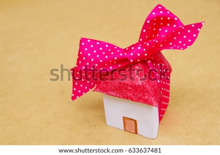 Little beautiful paper house with pink with white points ribbon on wooden background