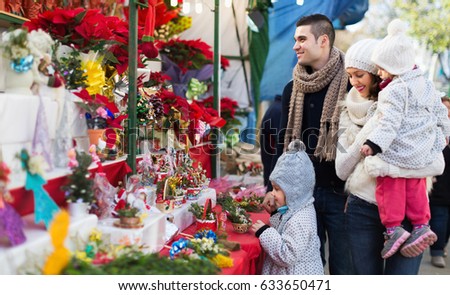 Smiling parents and children buying red Euphorbia at Christmas fair. Focus on man