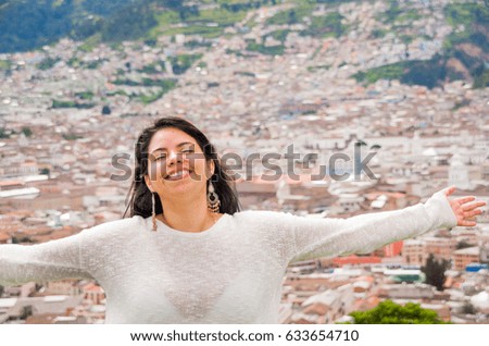 Latin freedom girl take the rays of sun over her face while she smiled happily when a colonial city is located behind her