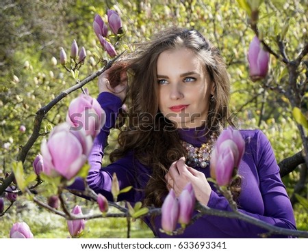 Girl face in magnolia flowers, hands near dark brown hair and on bust. Spring came, woman  in blooming garden smiling happy lucky lovely mood. Wavy crispy curly locks.                               