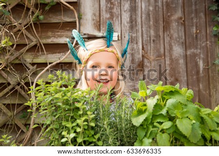 Happy little girl in colorful Indian headband standing in the garden surrounding by fresh green herbs