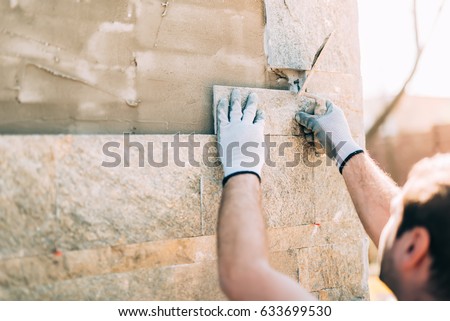 mason worker installing stone tiles on wall on construction site Royalty-Free Stock Photo #633699530
