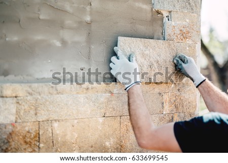 Construction worker installing stone on architectural facade of new building. details of construction industry Royalty-Free Stock Photo #633699545