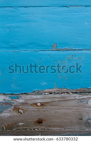 A blue, wooden surface with neglected boards of timber showing peeling paint and bare wood beneath in a textured background image.