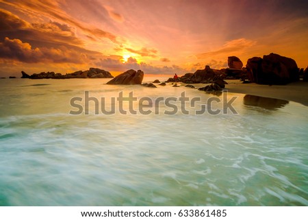 Soft wave of the sea on the sandy beach. Natural sunrise and rock island as background at Pantai Penunjuk ,Malaysia. Image contain grain and motion blur effect