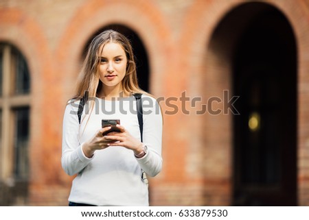 Gorgeous happy student holding notebooks texting on campus at college