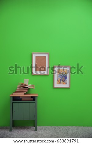 Bedside table with books and paintings on greenery wall background
