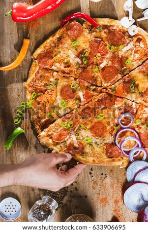 Hand taking slice of italian pizza with pepperoni on wooden table. Top view 