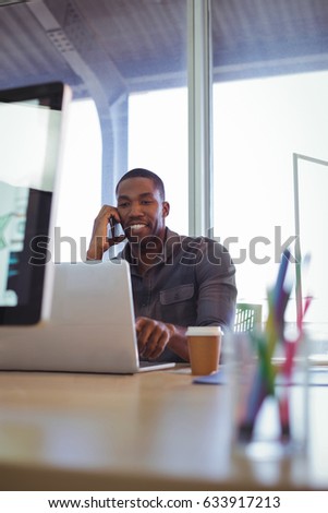 Smiling businessman talking on phone while working in creative office