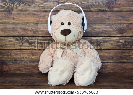 One brown teddy bear listens to music in white headphones, sits on a wooden brown background with a place for an inscription