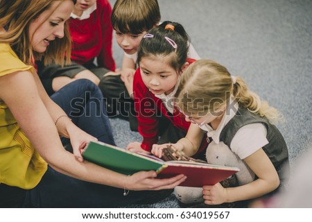 Teacher is sitting in the classroom with her primary school students, reading a story to them. Royalty-Free Stock Photo #634019567
