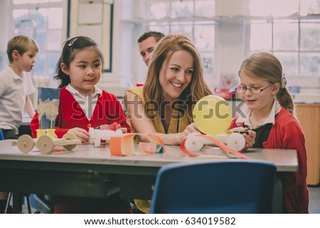 Primary school teacher is helping two of her students with a STEM project. They are building something using recycled items and crafts equipment.  Royalty-Free Stock Photo #634019582