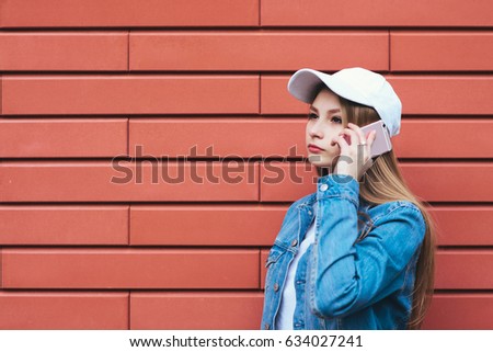 Outdoor portrait hipsterascho girl talking on the phone on a bright background. Stylish blonde woman in a denim jacket and cap talking on the phone in the background