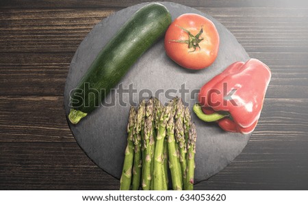 top view of delicious fresh zucchini, ripe tomato, green asparagus and sweet pepper on slate plate on rustic wood table