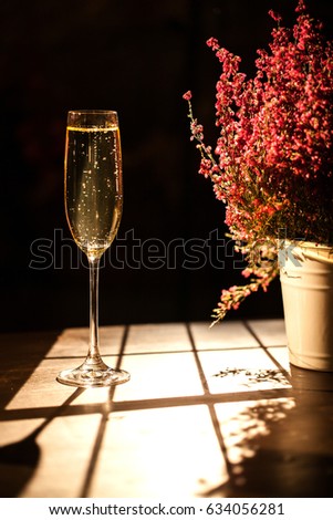 Vertical shot of champagne glass placed next to the flower pot on a wooden table.