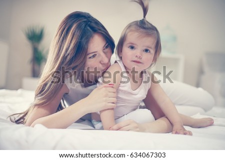 Young mother sitting with her baby on bed. Mother and little baby spending time at home.