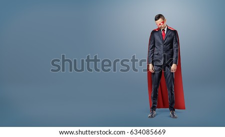 A sad businessman in a superhero red cape standing on dark blue background with his shoulders slumped. Business and risk. Failure and doubt. Unexpected trouble.