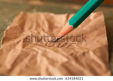 The pencil writes the word love on a paper.